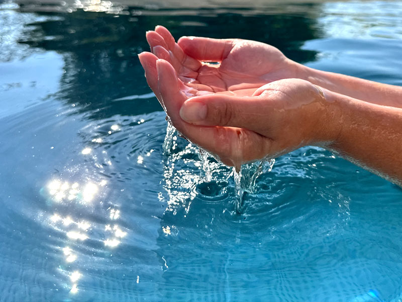 mains_dans_leau_de_-la-piscine Pureté de l'eau tenue dans les deux mains au dessus d'une piscine en inox